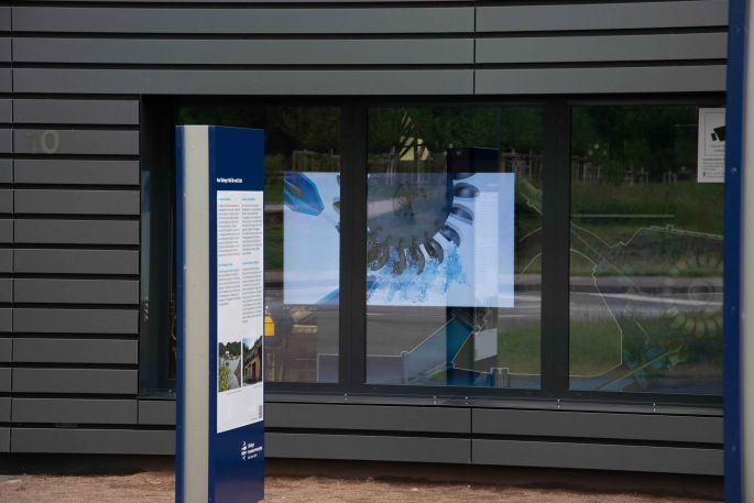 Ein Bildschirm im Schaufenster der Wasserkraftanlage zeigt Informationen zur Pelton-Turbine