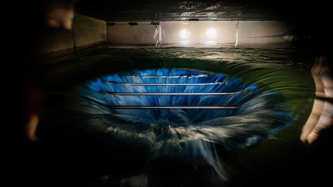 Wasser läuft über einen Überlauftrichter in einer Schwallwasserkammer einer Wasserkraftanlage